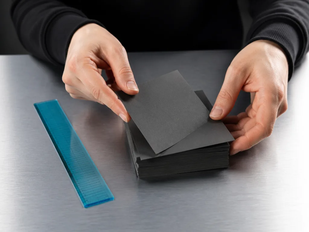Photorealistic editorial photograph of a player's hands sorting a stack of blank cardboard cards on a brushed aluminium